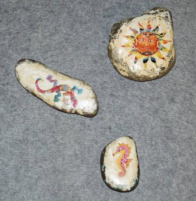 Bunte Steine mit gemalten Sonnensymbolen und fantasievollen Mustern.