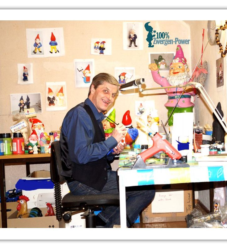 Andreas Klein sitzt an einem Tisch und bemalt Zwergenfiguren in einem dekorierten Raum.